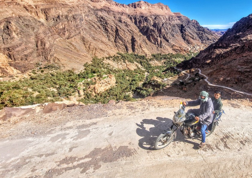A rider pushing a loaded bike up a switchback in a deep canyon.