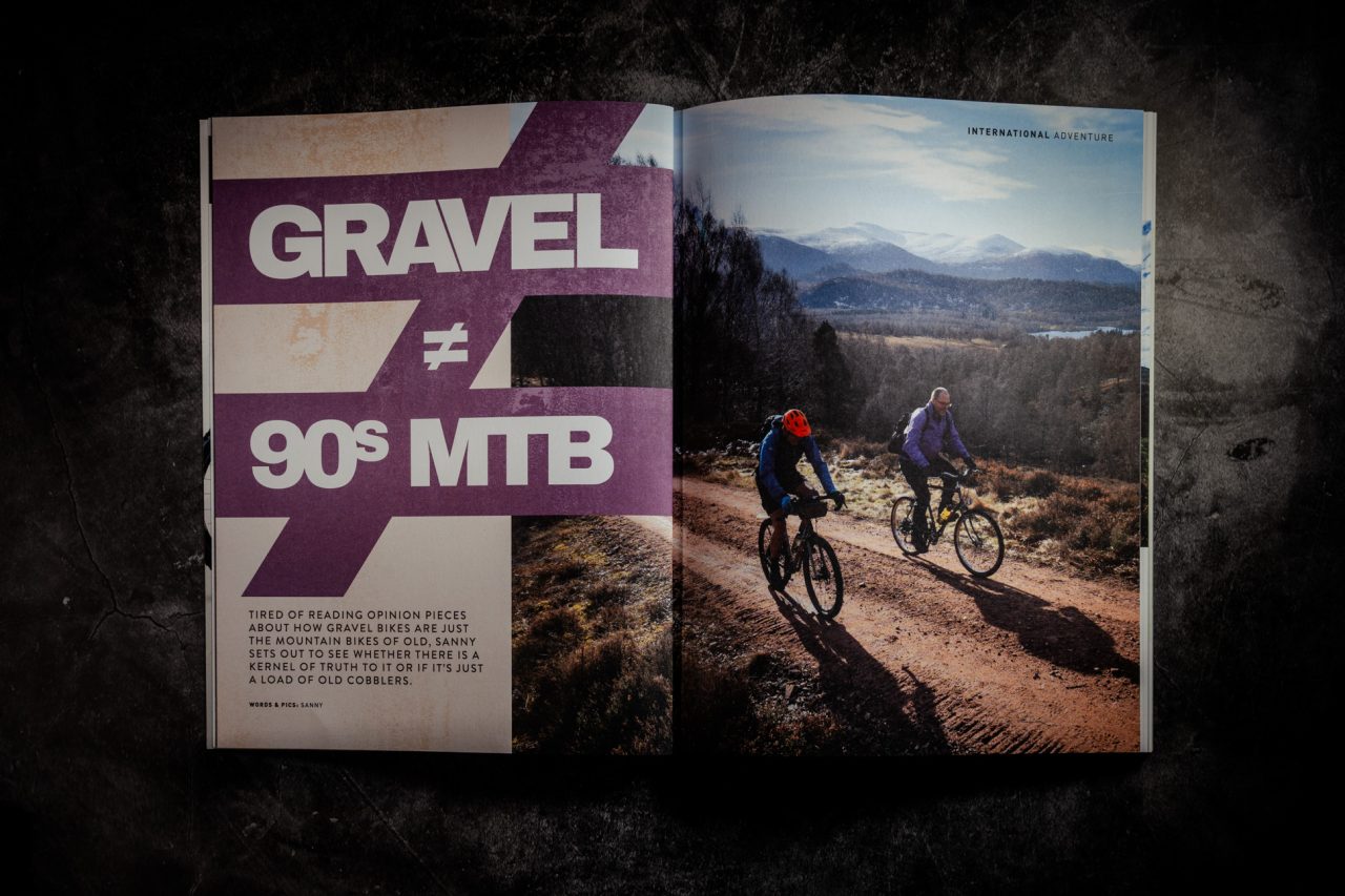 Double-page spread of 'Gravel โ 90s MTB' from Singletrack Magazine Issue 167, showing two cyclists with backpacks on a gravel track with snow-capped hills in the distance