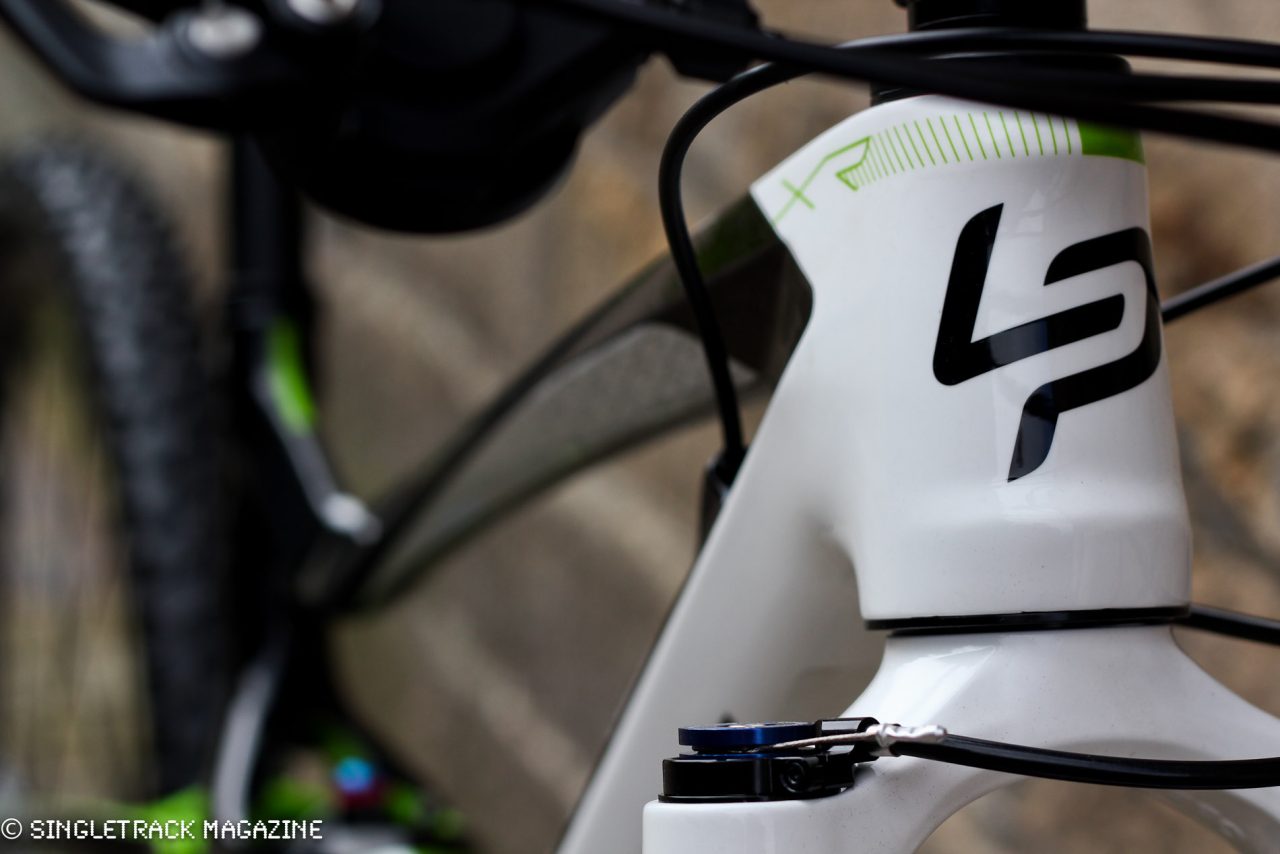 Close-up of a mountain bike frame displaying the logo and design features, with a focus on the head tube and cables.