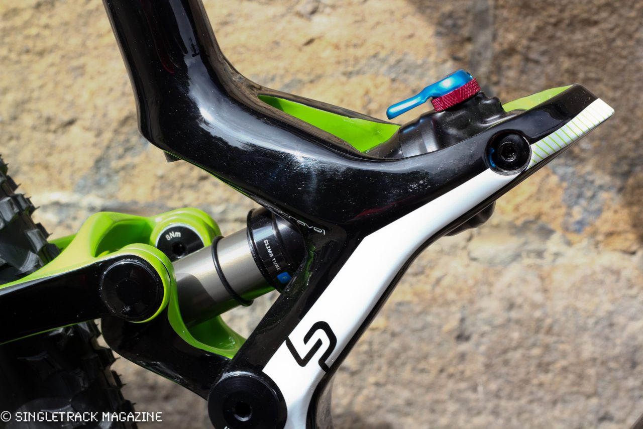Close-up of a mountain bike's rear suspension, featuring a combination of black and green components, with highlighted adjustment knobs.