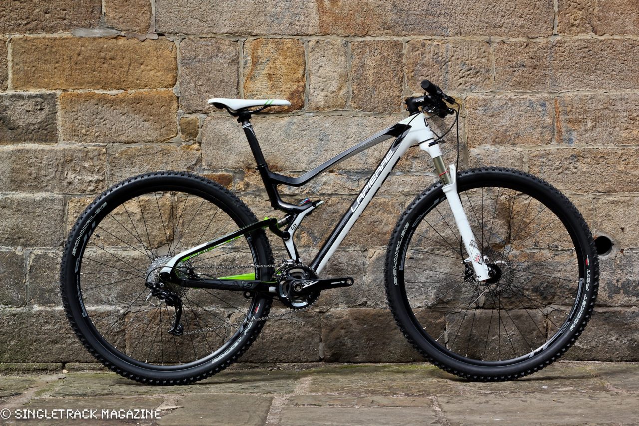 A mountain bike with a black and white frame, featuring green accents, positioned against a stone wall.