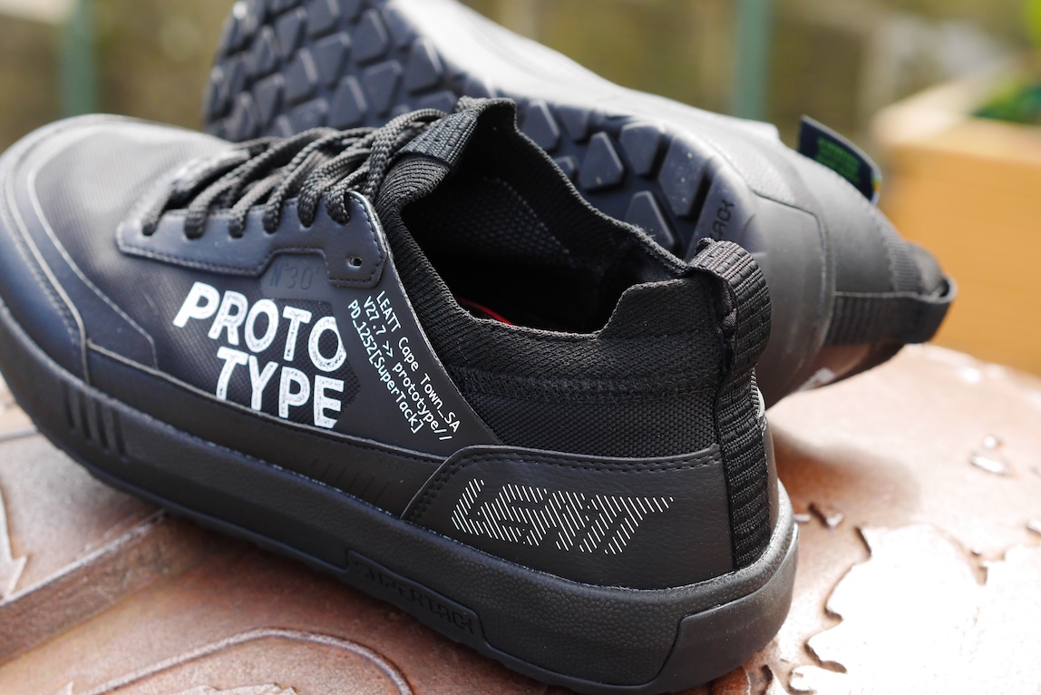 Close-up of black LEATT prototype shoes with branding details, focusing on the textured sole and design elements.