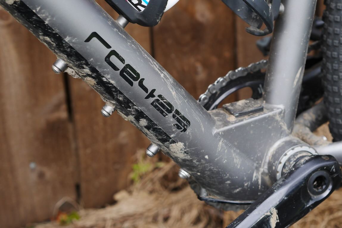 Close-up of a muddy bicycle frame showing the brand logo and components.