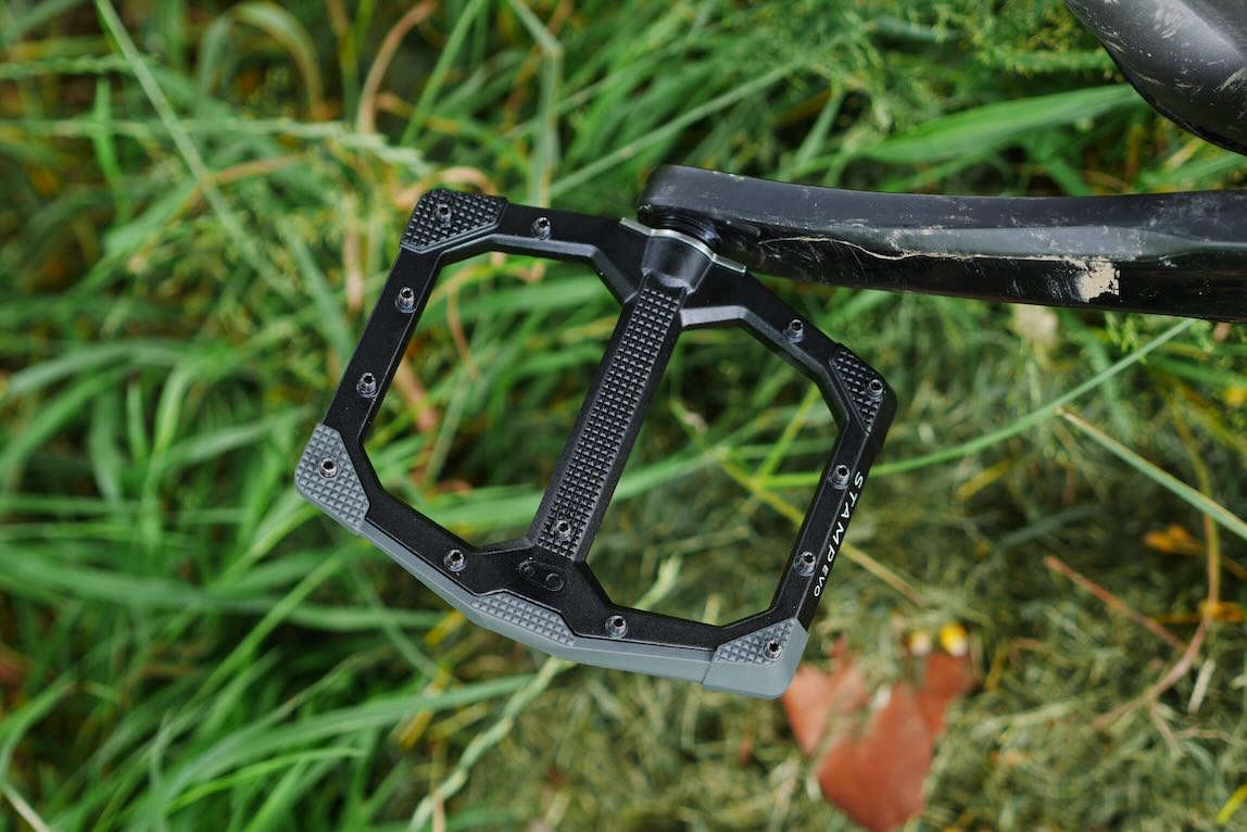 Close-up of a black bicycle pedal resting on grass, showing textured surface and design details.