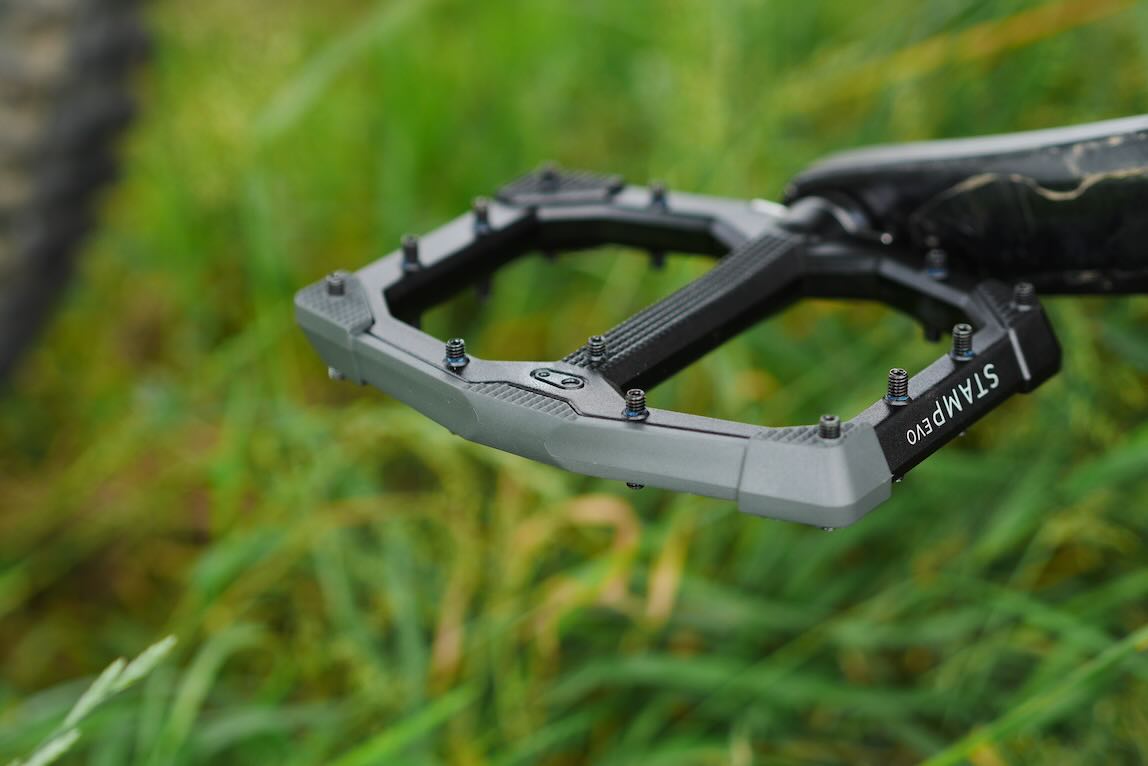 Close-up of a bike pedal resting on green grass, showcasing its textured surface and grip pins.