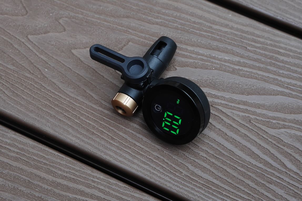 A digital pressure gauge with a black body and green LED display, resting on a textured wooden surface.