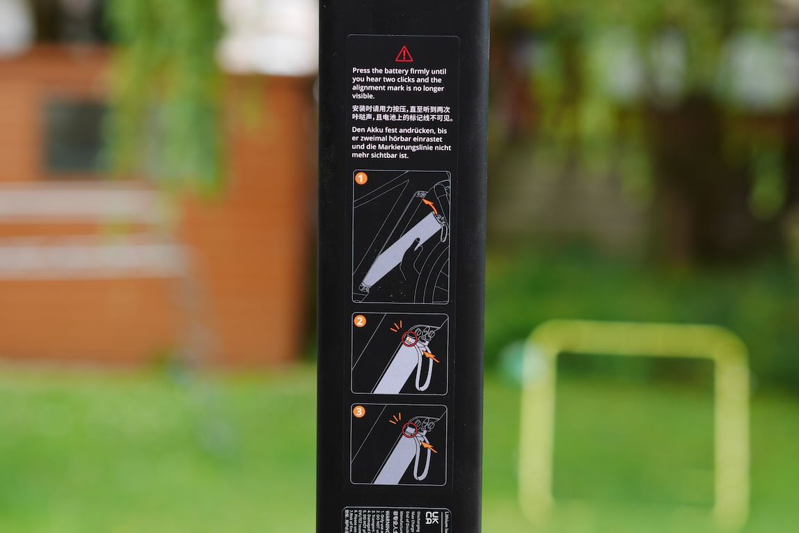 Instruction panel showing battery installation steps with illustrations, set against a blurred outdoor background.