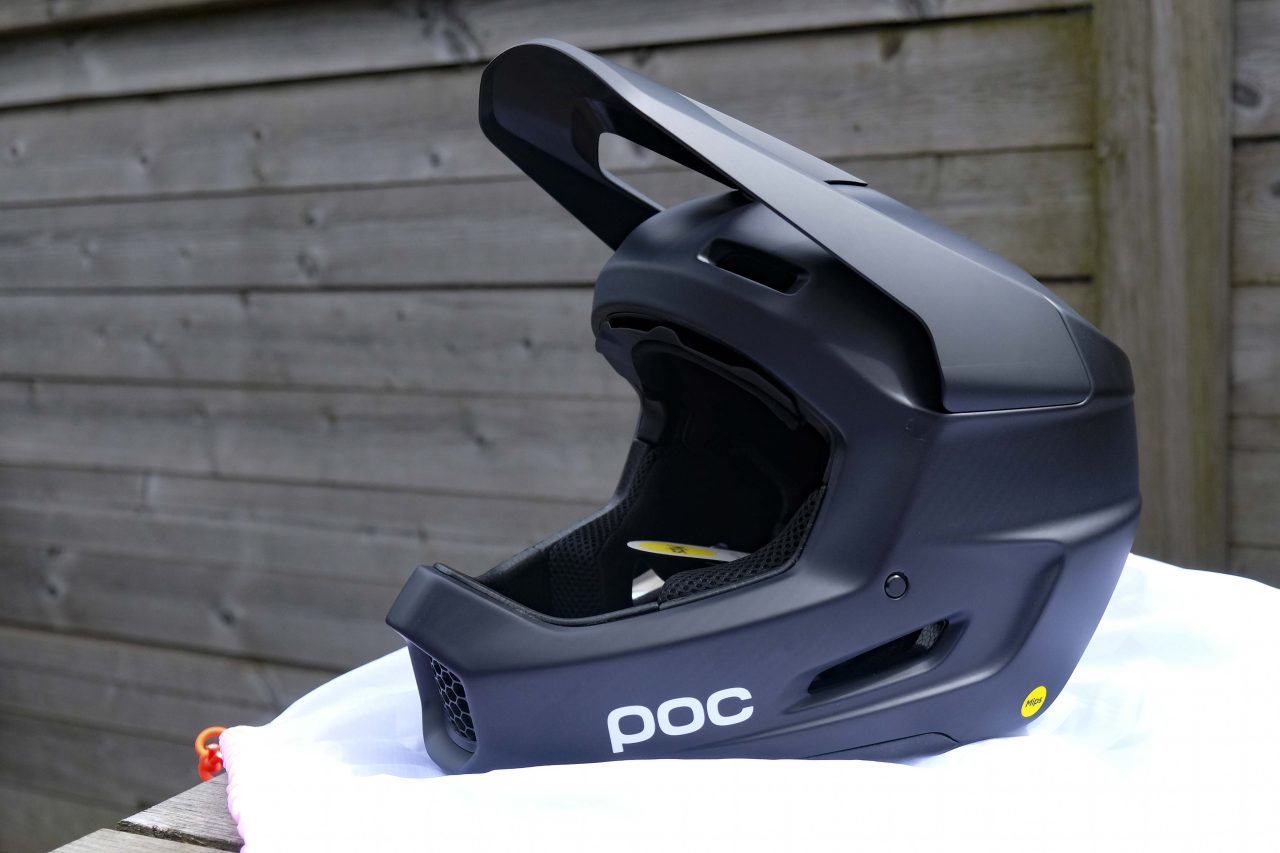 A black POC bike helmet displayed on a white surface with a wooden fence in the background.