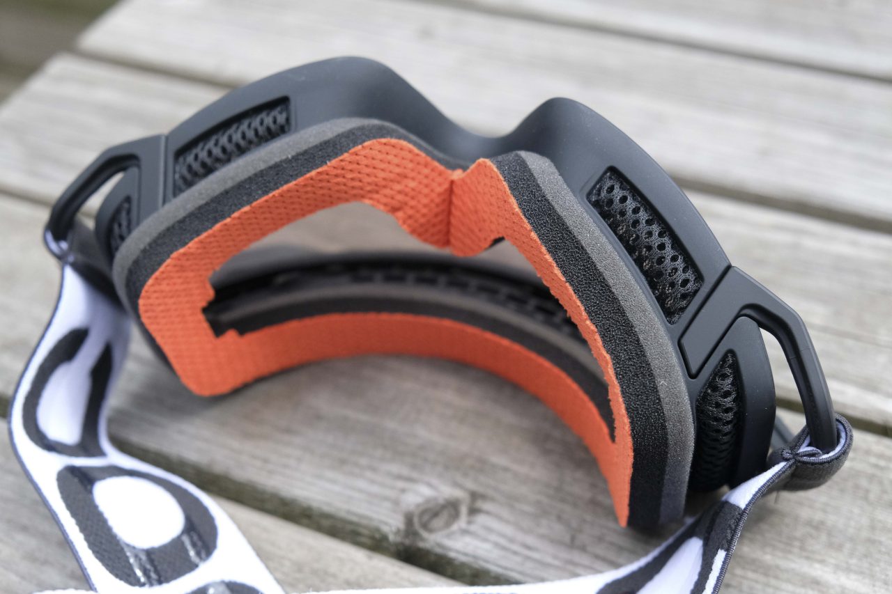 Close-up view of a black and orange ski goggle, highlighting the inner foam cushion and strap on a wooden surface.