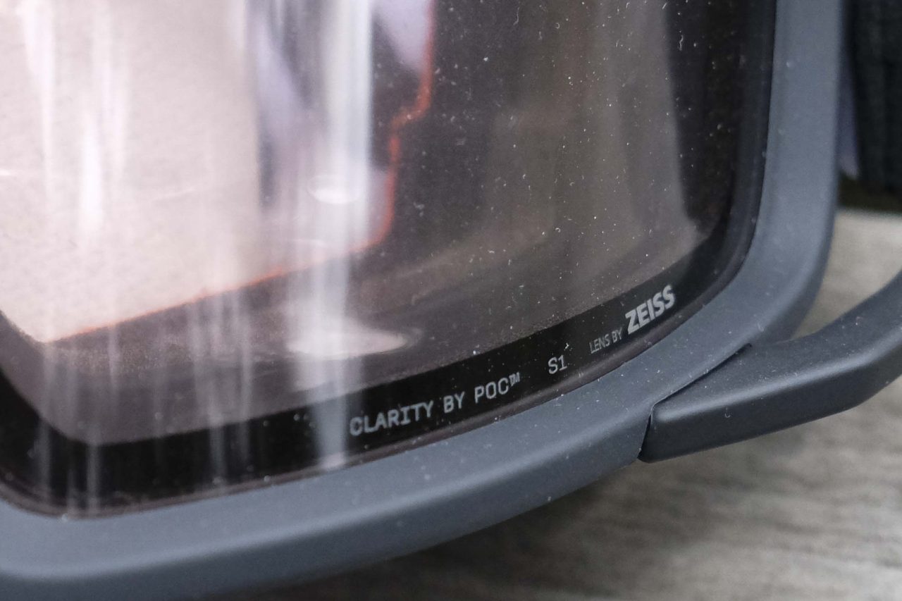 Close-up of a ski goggles lens showing the text 'CLARITY BY POC', 'S1', and 'LENS BY ZEISS' on the lower edge.