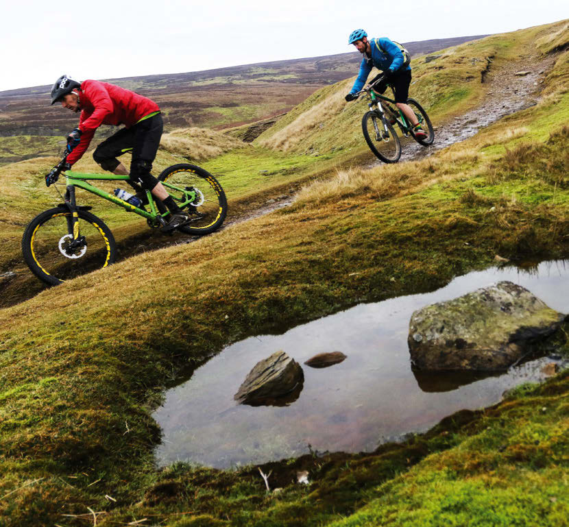 A rider descends Fremington Edge past puddles on the grassy bridleway with Swaledale stretching out behind