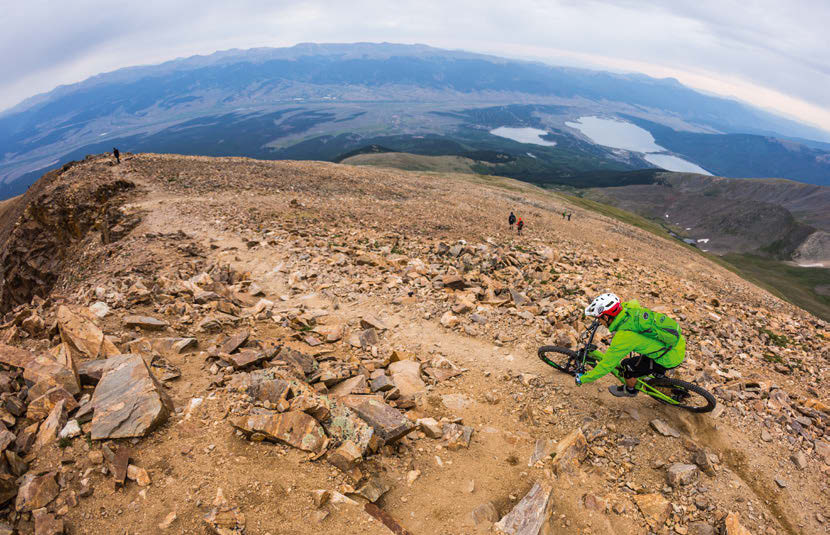 A rider descends the flowing singletrack from the summit of Mount Elbert towards the lakes below