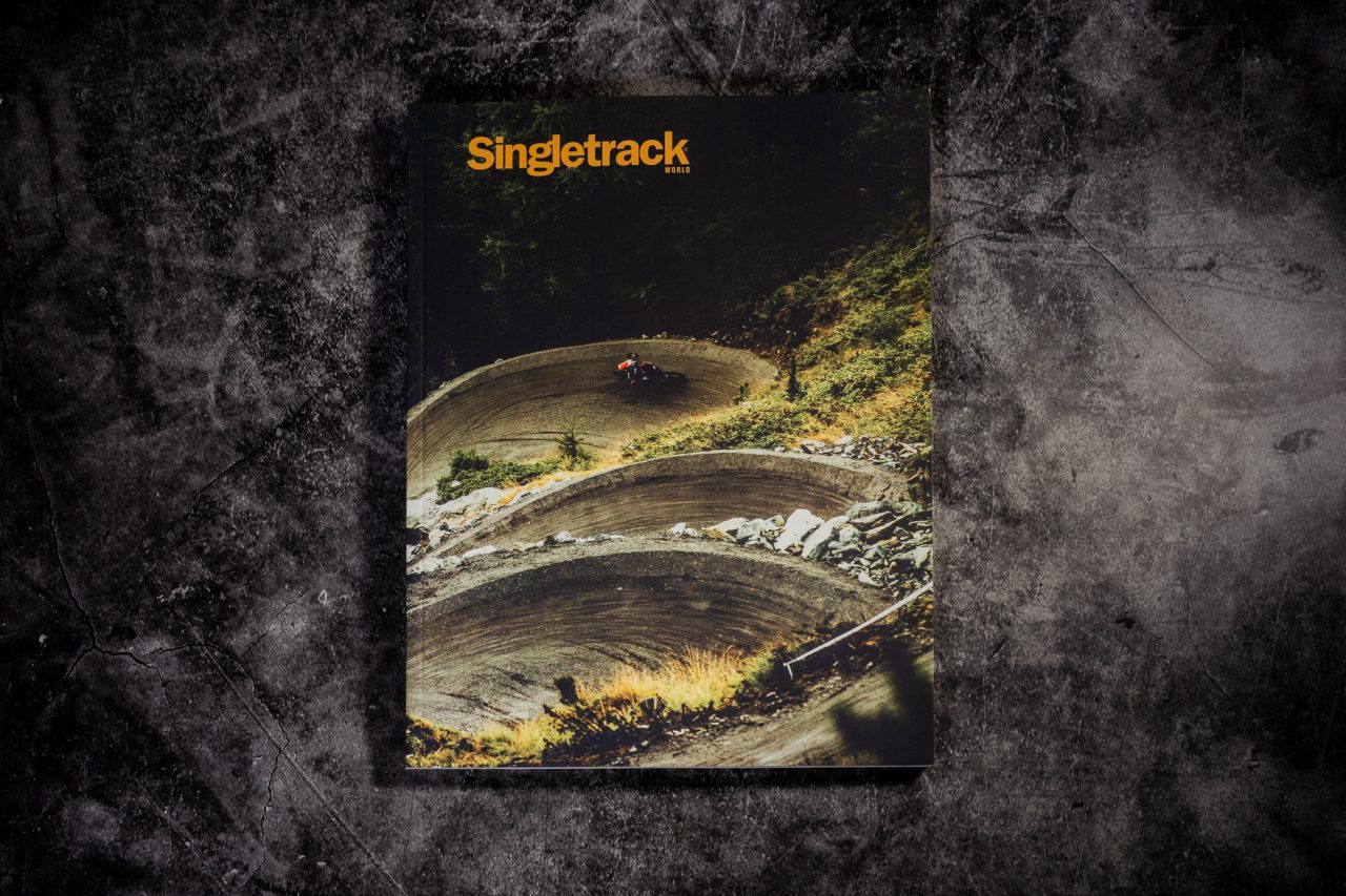 Cover of the magazine 'Singletrack' featuring a winding trail with a cyclist in a lush green setting.