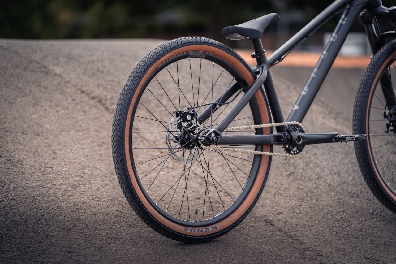 Close-up of a bicycle's rear wheel, featuring a textured black tyre with a brown sidewall and a well-maintained chain and gearing system.
