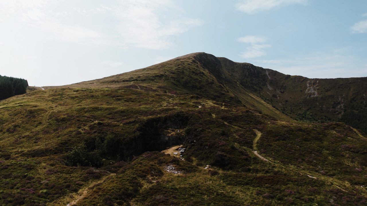 A scenic view of a green hillside leading to a rocky mountain peak under a clear blue sky.