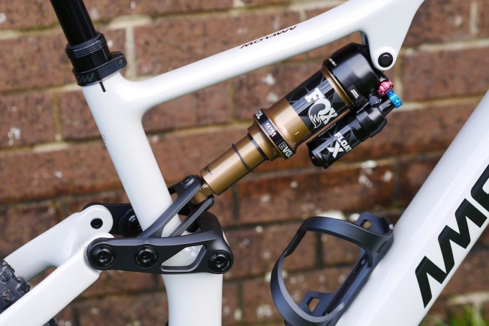 Close-up of a mountain bike's rear shock absorber mounted on a white frame against a brick wall.