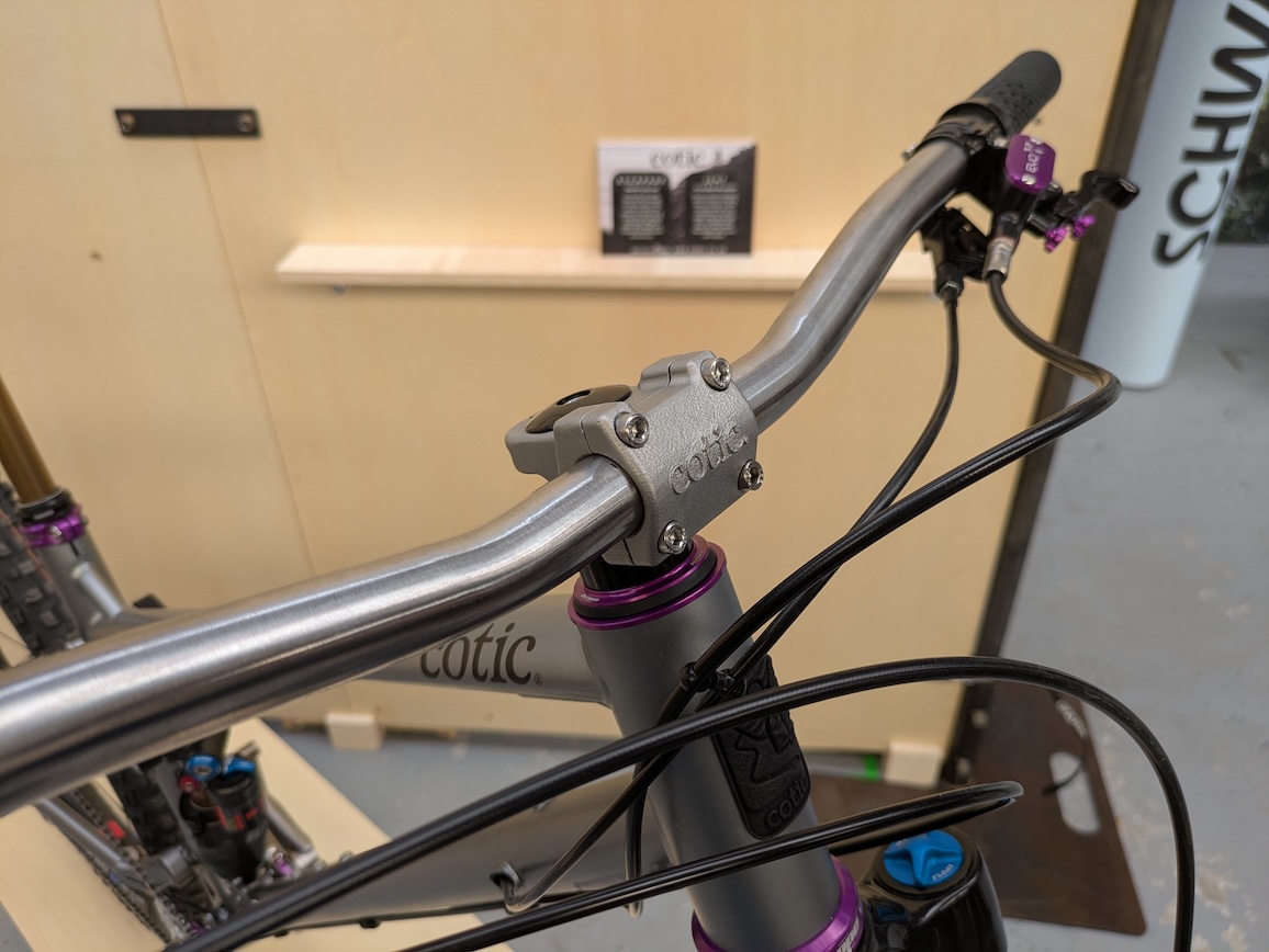 Close-up view of a Cotic mountain bike handlebar and stem, showcasing a sleek silver finish and purple accents.
