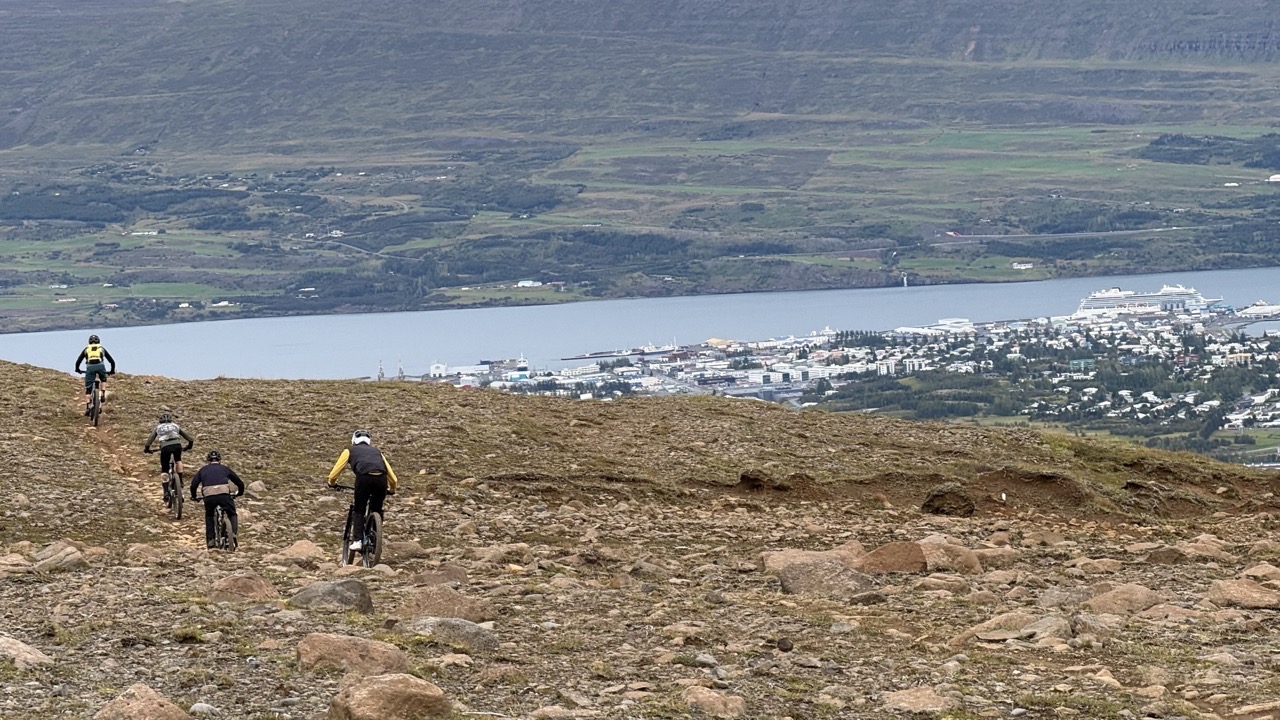 A group of mountain bikers descending a rocky trail with a coastal town and water in the background.