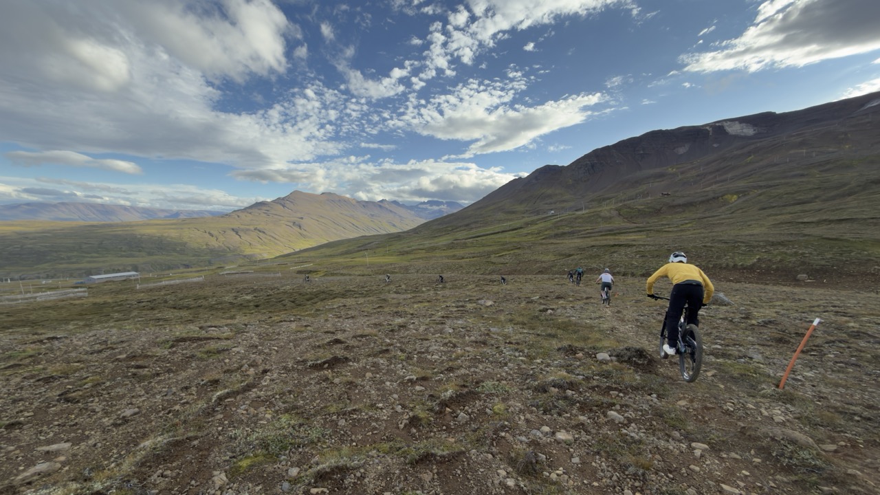 Mountain bikers riding on a rocky trail in a mountainous landscape with clouds in the sky.