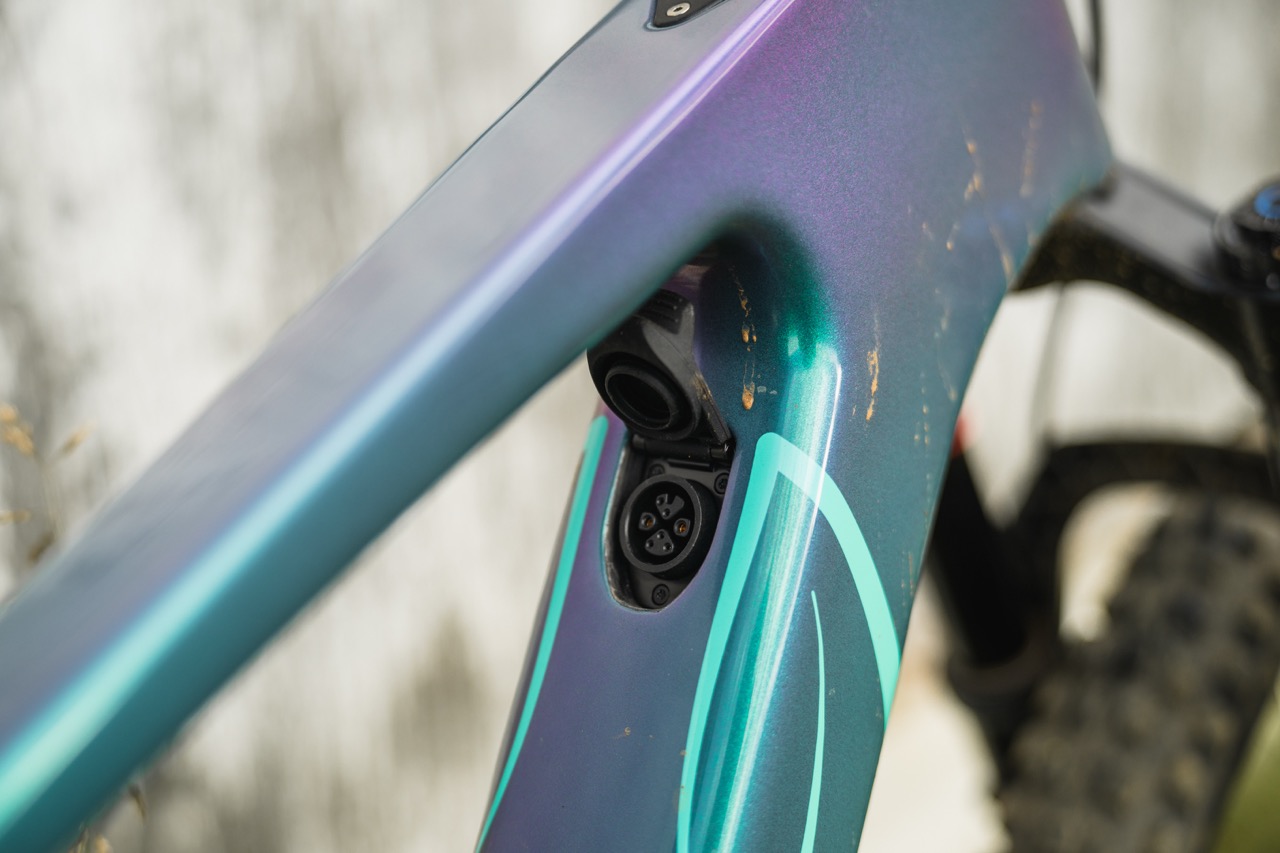 Close-up of a colourful bike frame showing a connector for electronic components, featuring scratches and a sleek design.